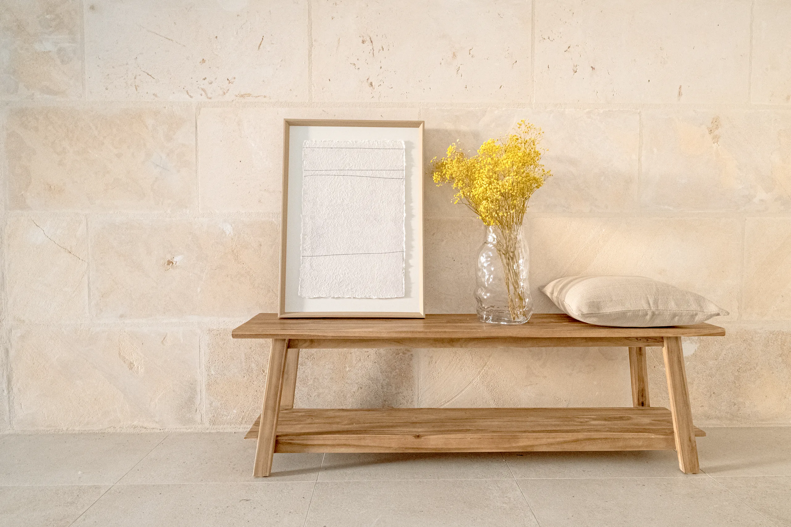 banco-teca-maciza-muro-mares-interiorismo-mallorca Banco de teca maciza con un cuadro, jarrón con flores secas y cojín junto a un muro de marés