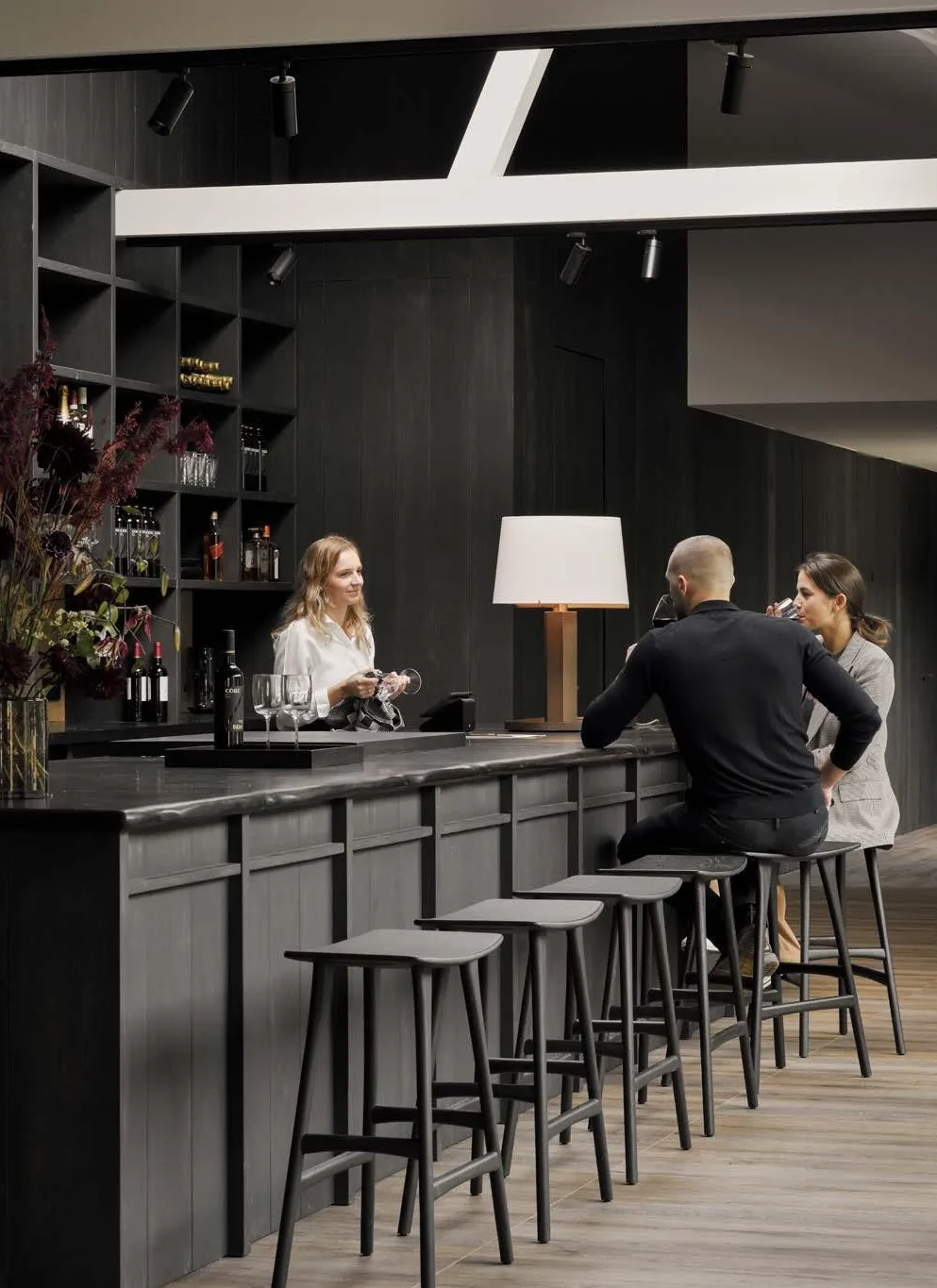 Barra de bar con taburetes y estanterías oscuras en un espacio de hostelería Barra de bar con taburetes y estanterías oscuras en un espacio de hostelería