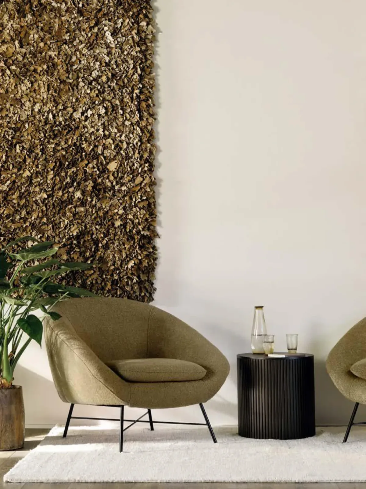 Butacas tapizadas en verde oliva con mesa auxiliar negra junto a un panel decorativo de fibras naturales.