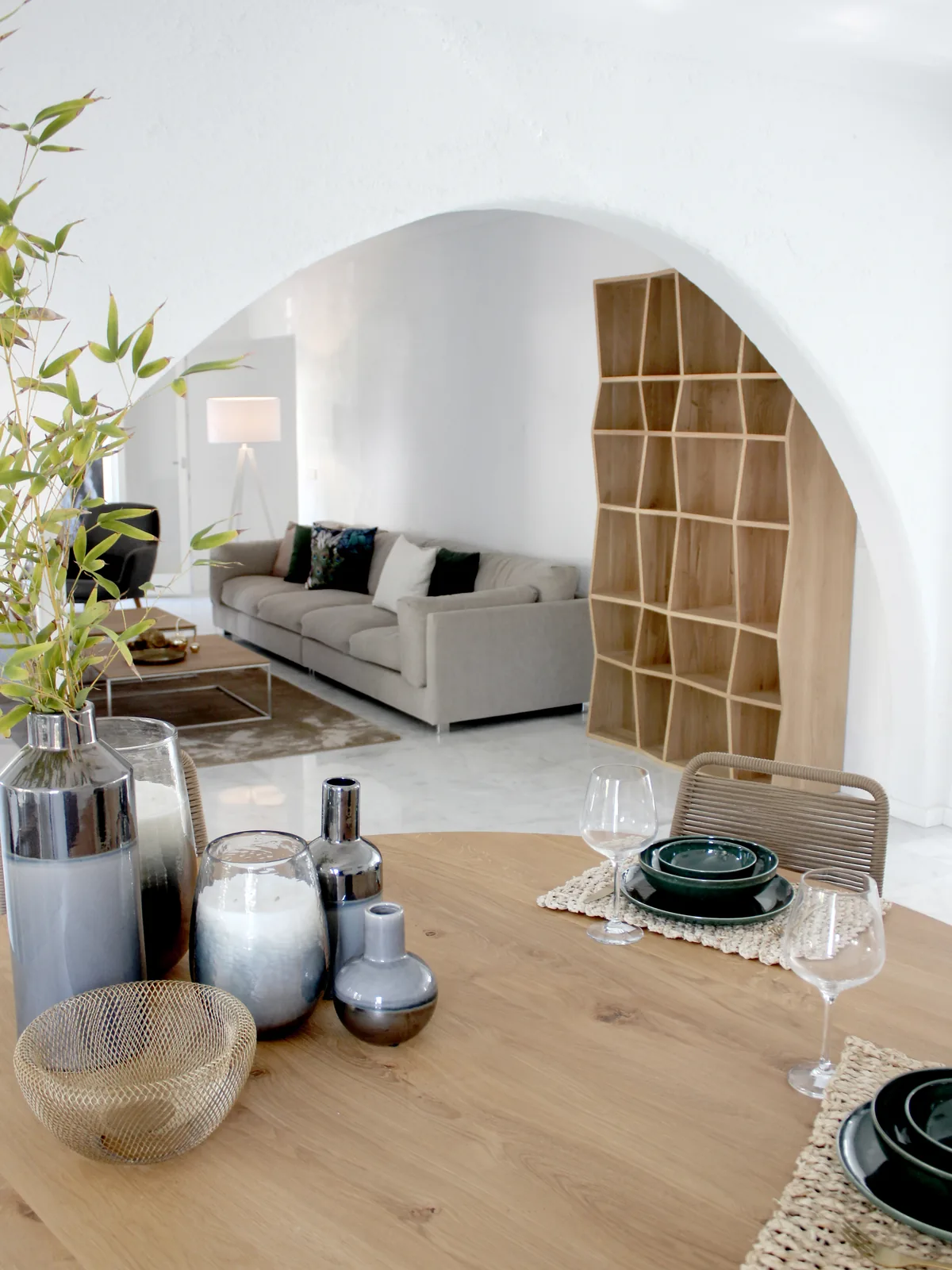 Comedor con mesa de roble puesta, jarrones de cristal y un arco que da al salón en una villa del Port d'Alcúdia.