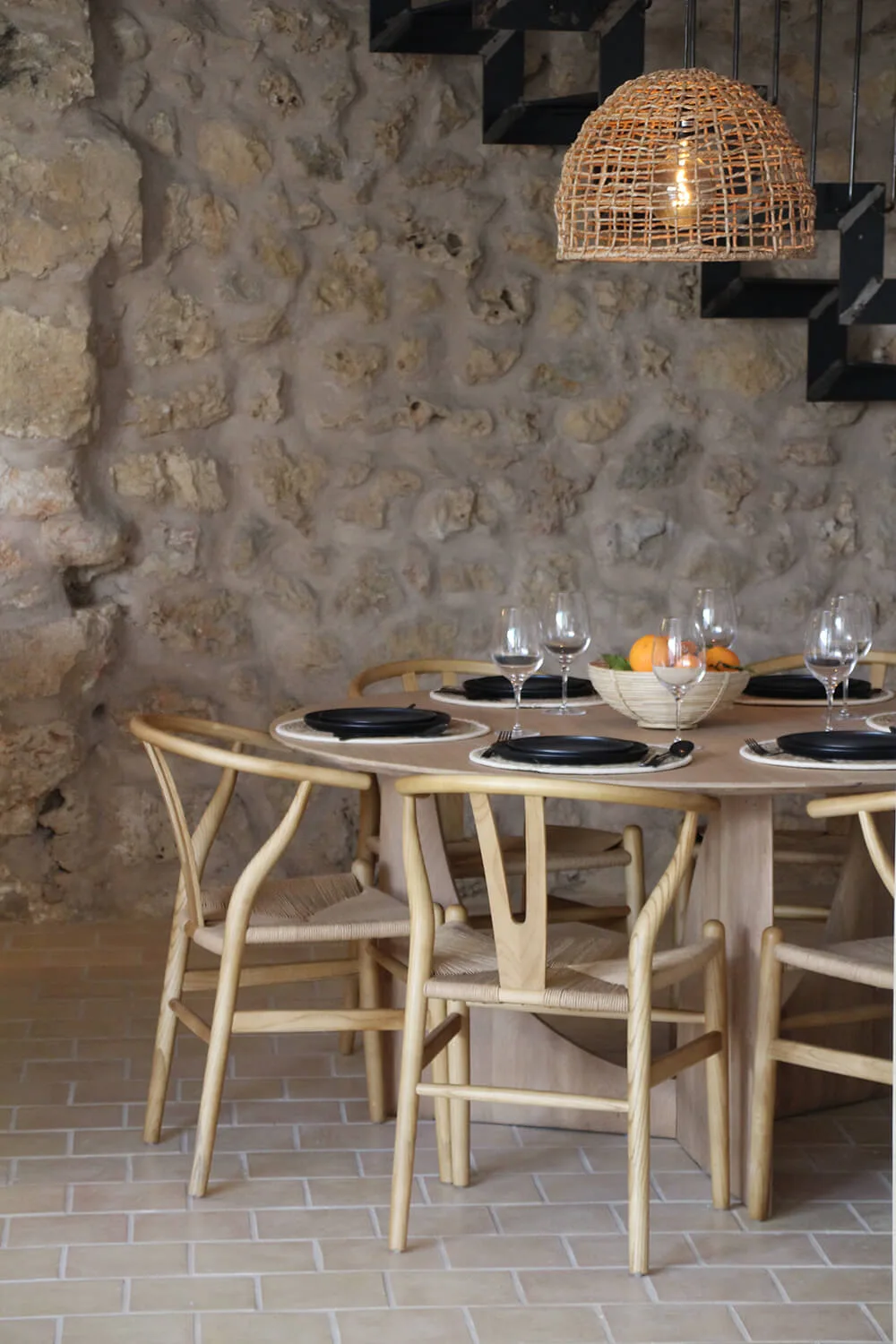 Essbereich mit Natursteinwand, rundem Tisch und Holzstühlen unter einer geflochtenen Pendelleuchte in einem Haus in Sineu