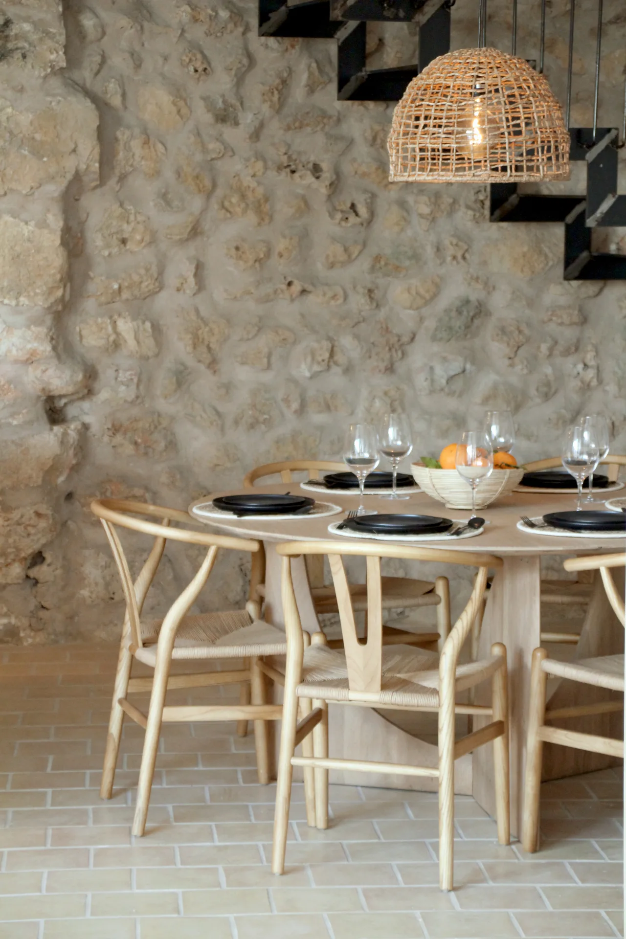 Comedor con sillas de madera y lámpara de fibra junto a una pared de piedra mallorquina