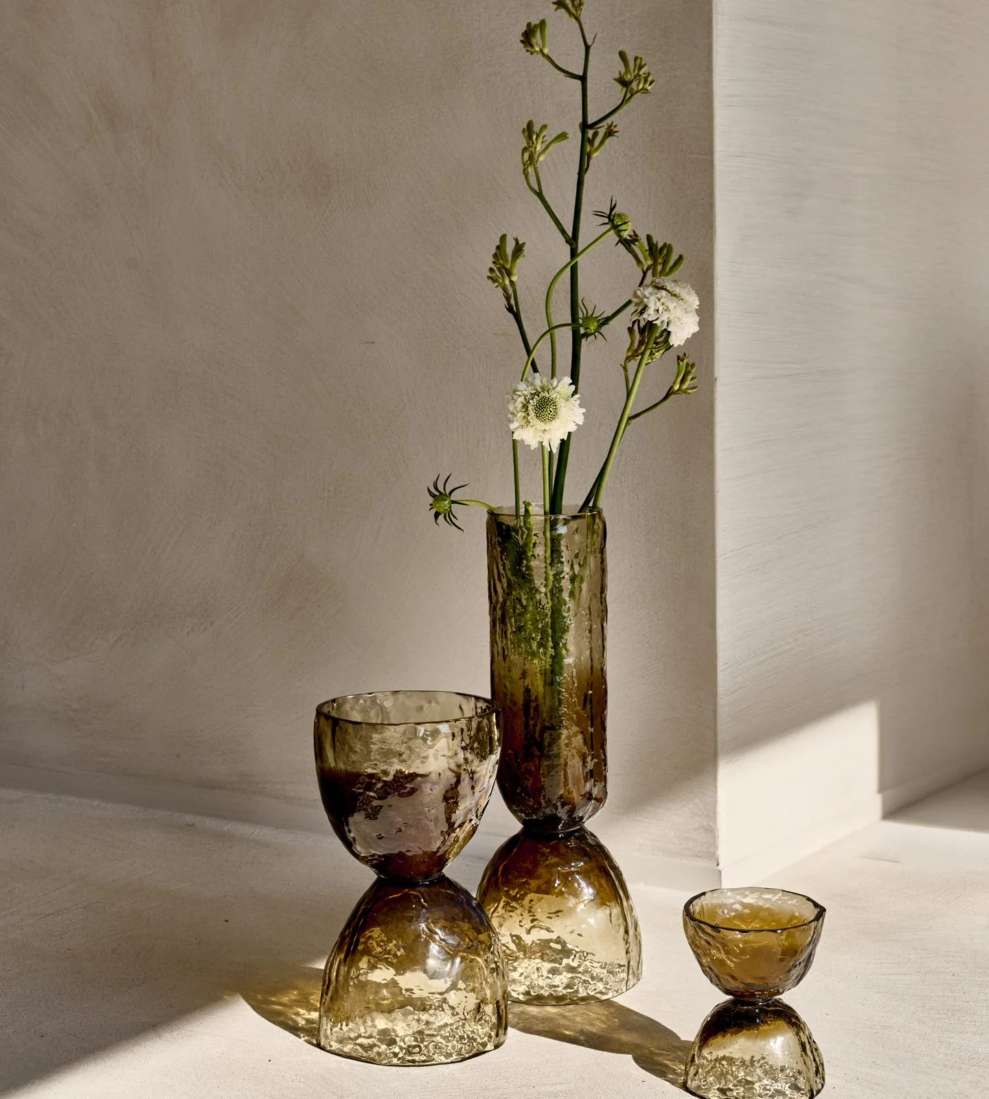 home-staging-piezas-cristal-decoracion Jarrones de cristal ámbar con flores silvestres sobre un suelo claro