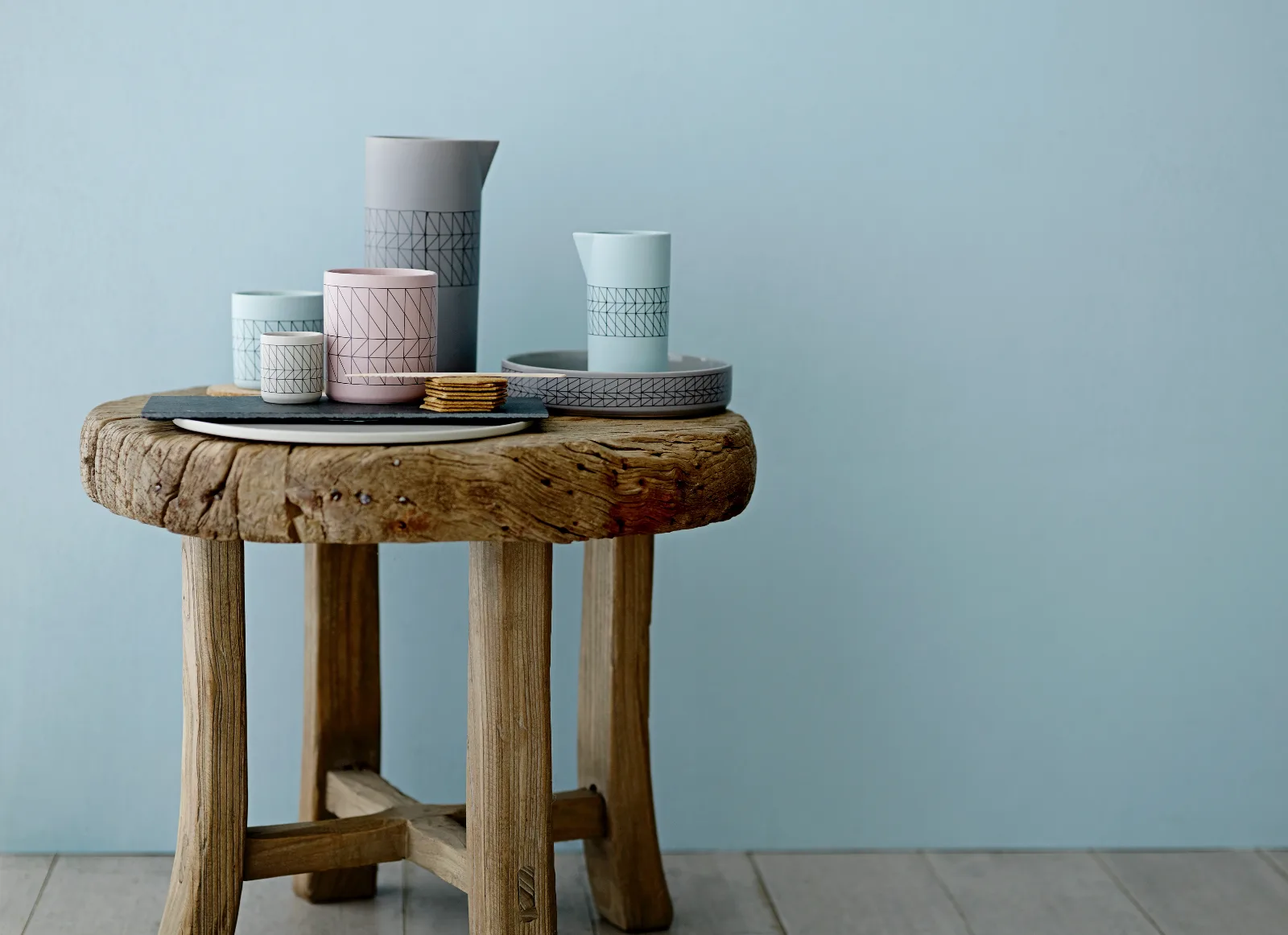 Holzhocker mit pastellfarbener Keramik vor einer hellblauen Wand