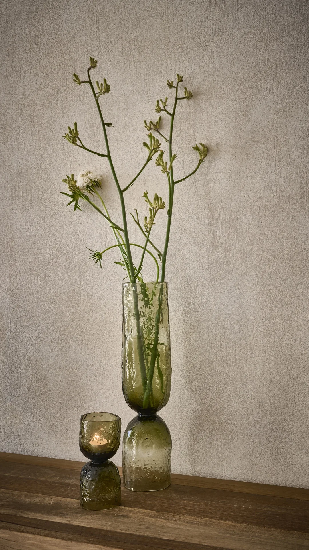Jarrón alto de vidrio con ramas en flor sobre un suelo de madera