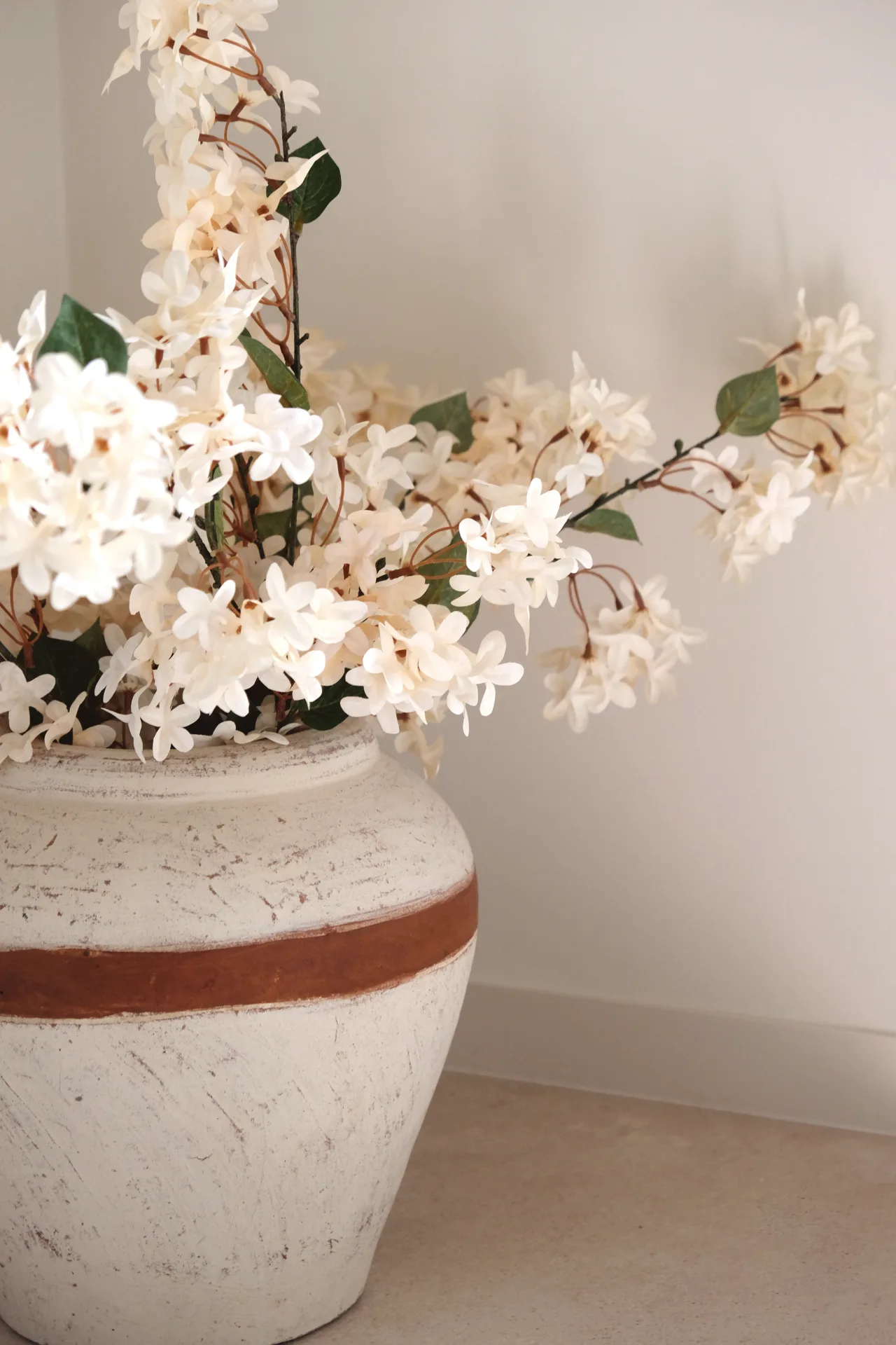 Jarrón de cerámica con flores blancas junto a una pared clara Jarrón de cerámica con flores blancas junto a una pared clara