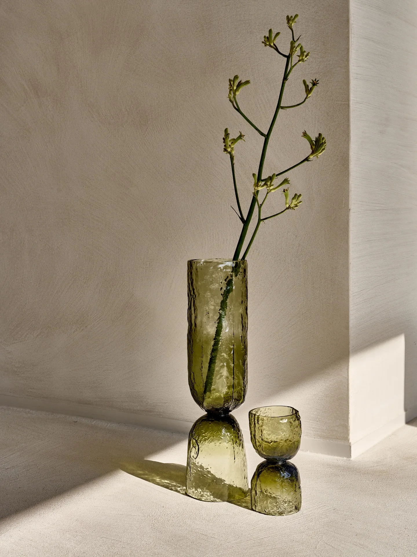 Jarrón de vidrio verde con una rama en flor junto a la pared