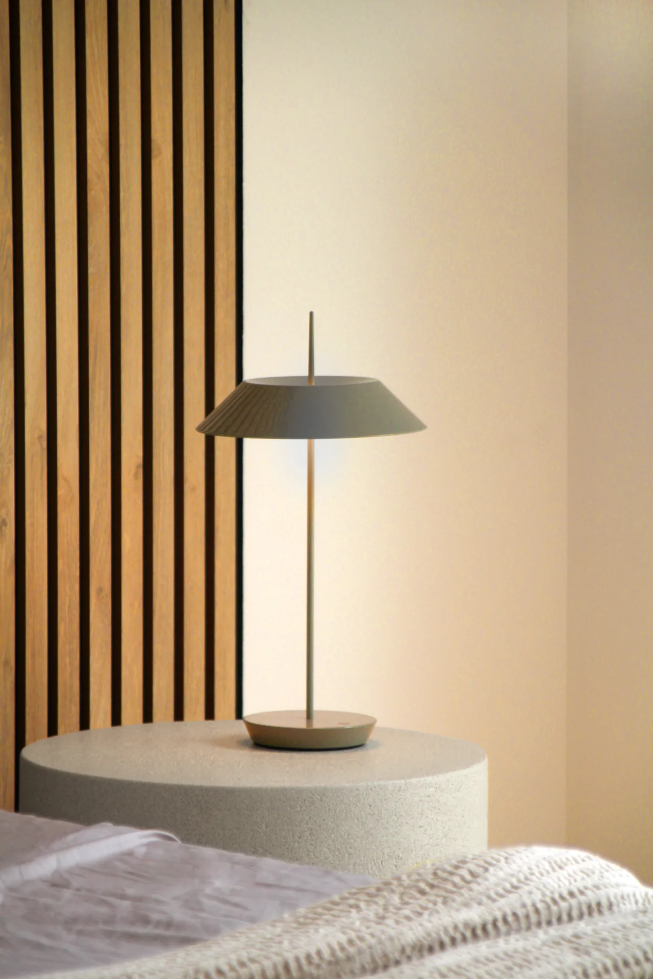 Lámpara de mesa sobre mesilla junto a un panel de listones de madera Lámpara de mesa sobre mesilla junto a un panel de listones de madera