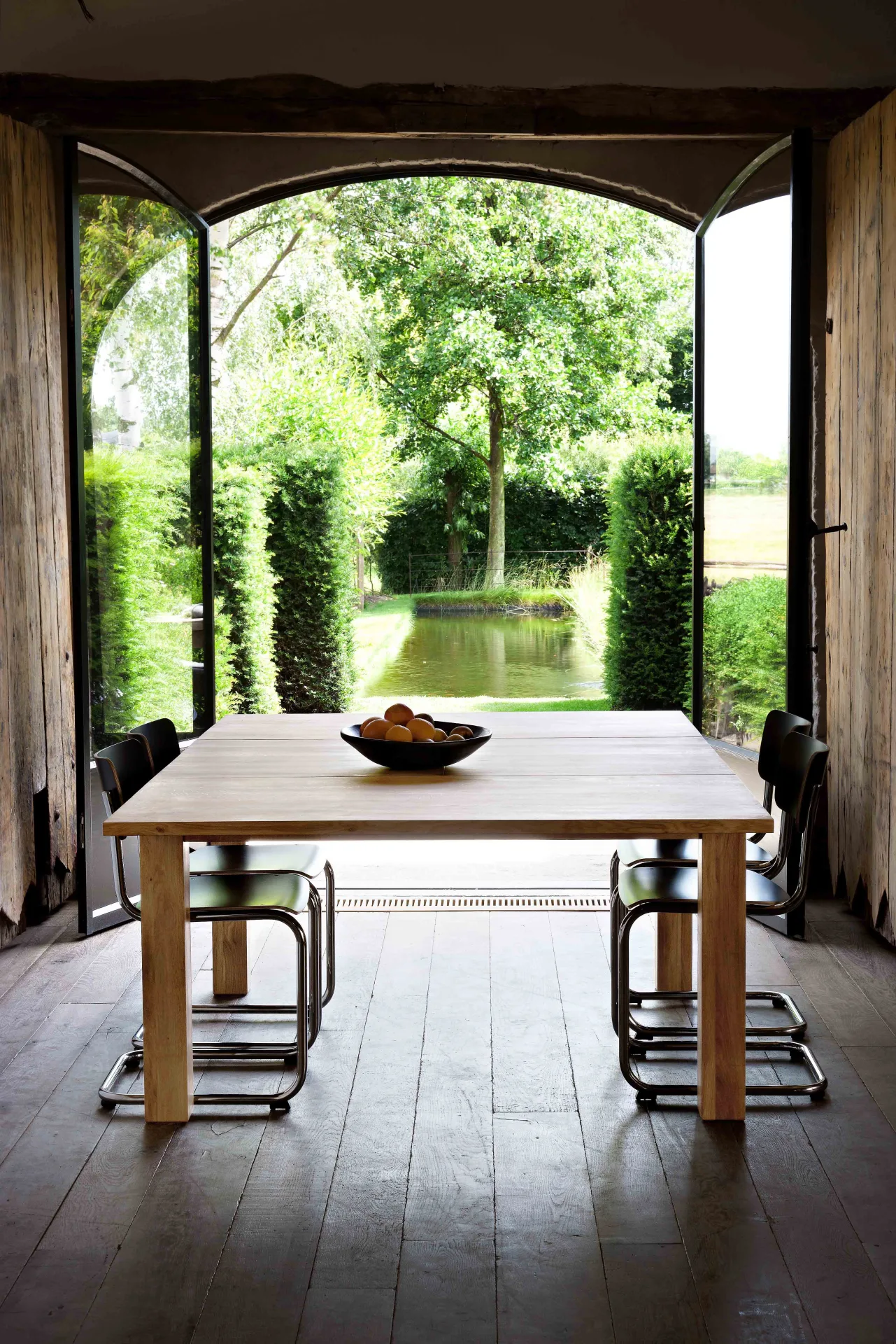 Square wooden dining table with chairs facing open garden doors