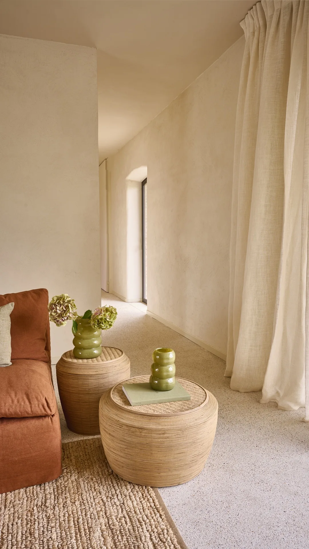 Pasillo luminoso con sofá terracota, mesas de fibra y cortinas de lino