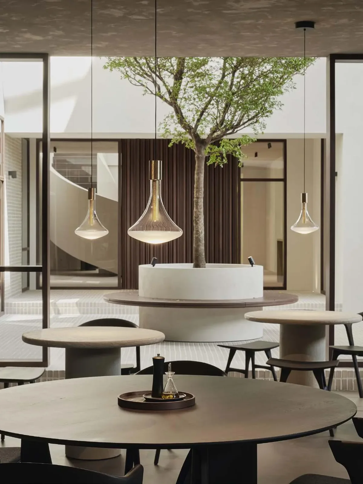 Restaurante con mesas redondas, lámparas colgantes de vidrio y un árbol en el centro de la sala.
