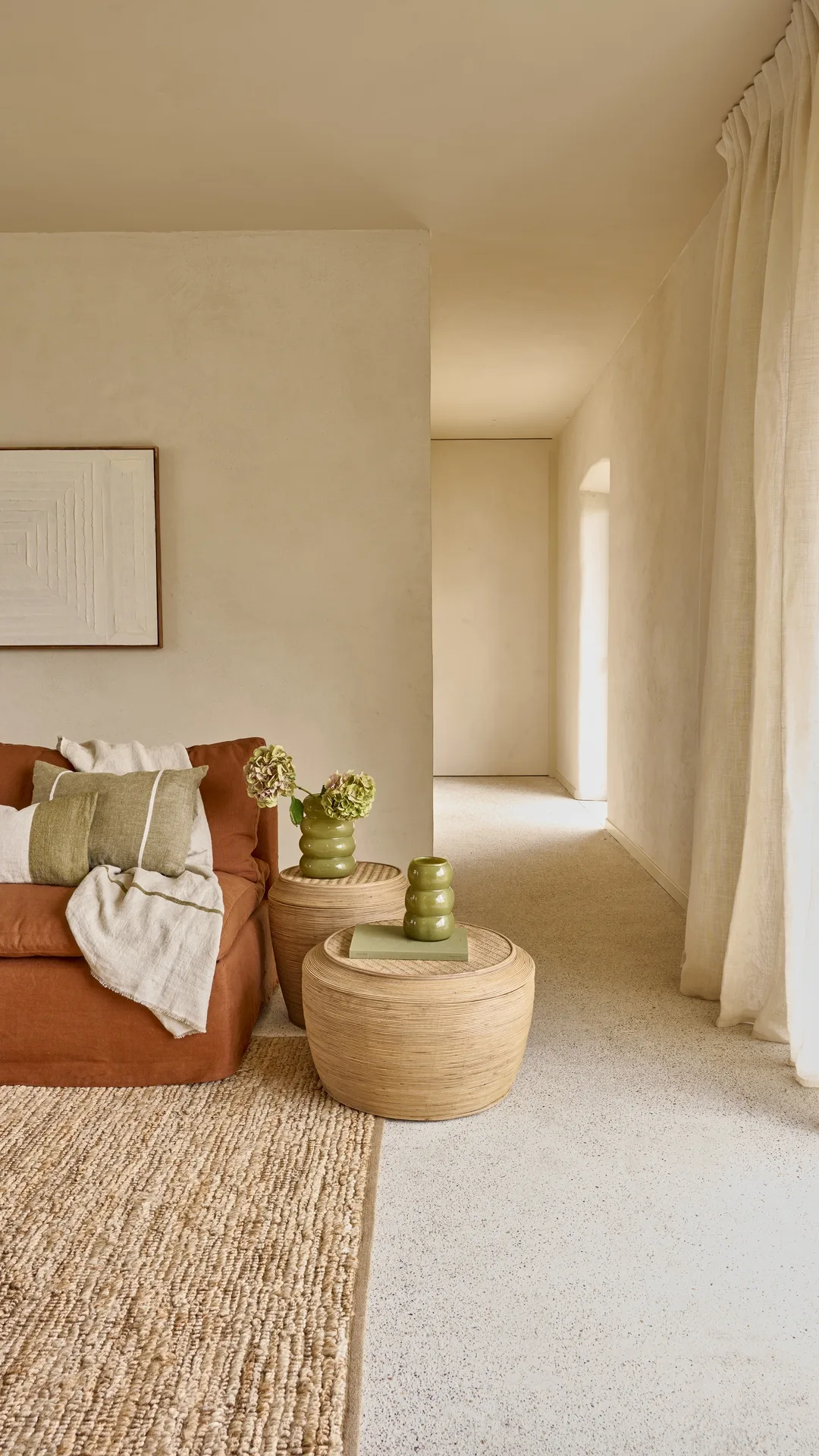 Rincón de salón con sofá terracota, mesas de fibra y cortinas de lino