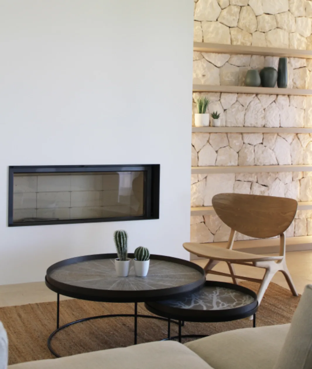 Wohnzimmer mit Kamin, Steinregalen, Holzsessel und runden Couchtischen