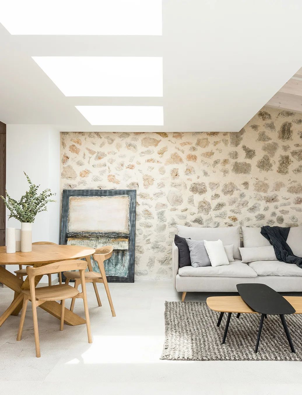 Wohn- und Essbereich mit Natursteinwand, grauem Sofa und Holztisch in einem Chalet in Pollença