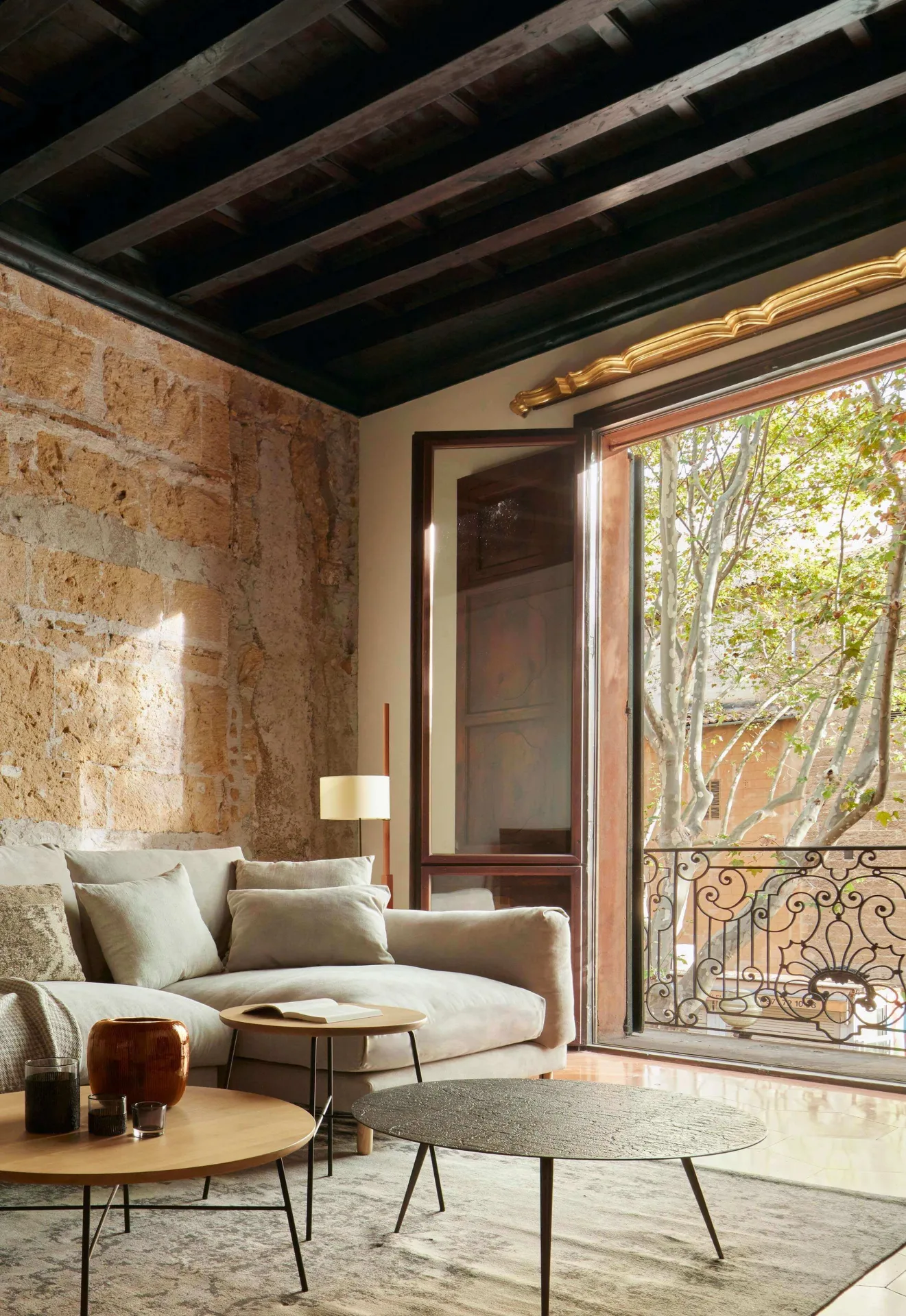 Wohnzimmer mit Marès-Steinwand, dunkler Balkendecke, hellem Sofa und Couchtischen in einer Wohnung in Palma
