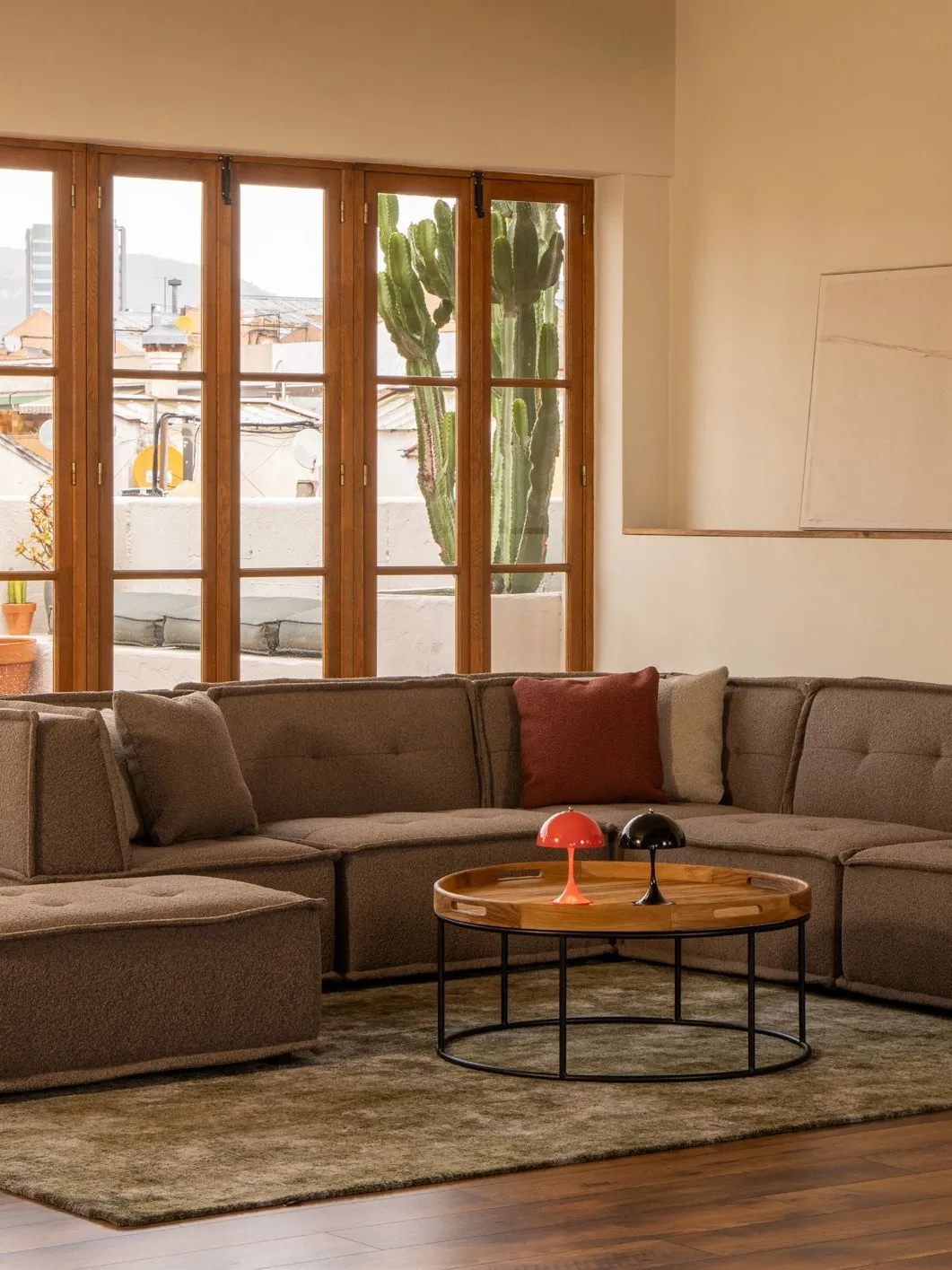 Salón con sofá modular, mesas redondas de madera y ventanales