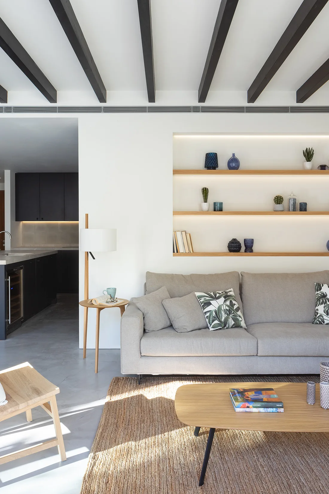 Salón con vigas oscuras, sofá gris, mesa de centro de roble y estanterías iluminadas en una casa de Son Espanyolet.