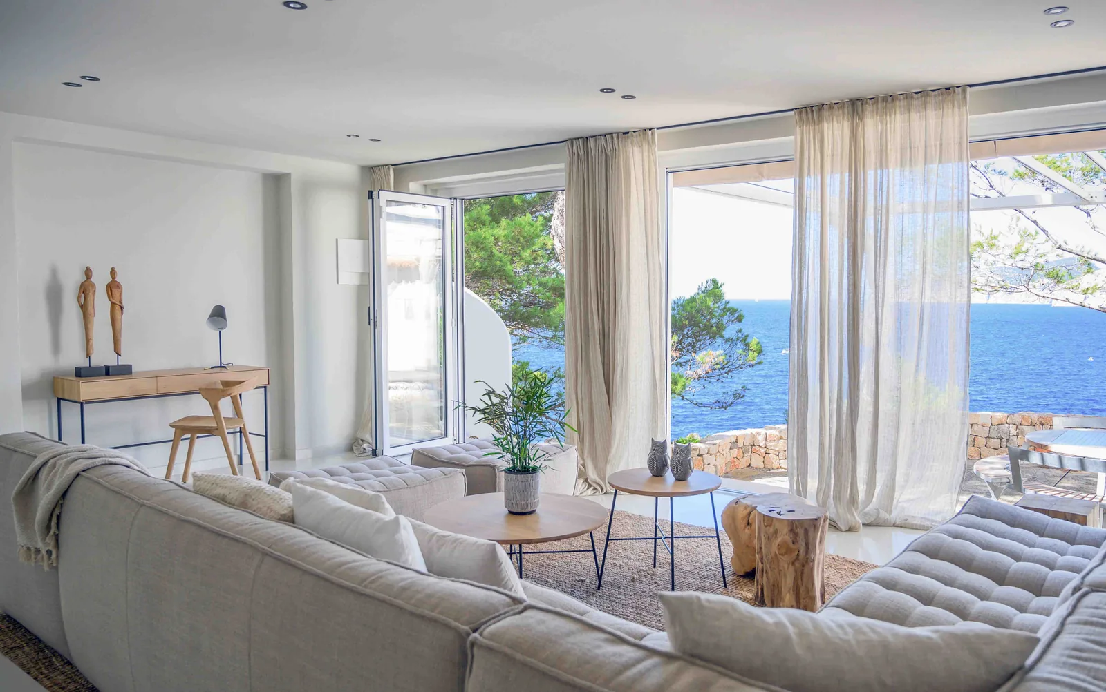 salon-vistas-mar-sofa-lino-casa-santa-ponca Salón con sofá de lino, cortinas vaporosas y grandes ventanales con vistas al mar en una casa de Santa Ponça.