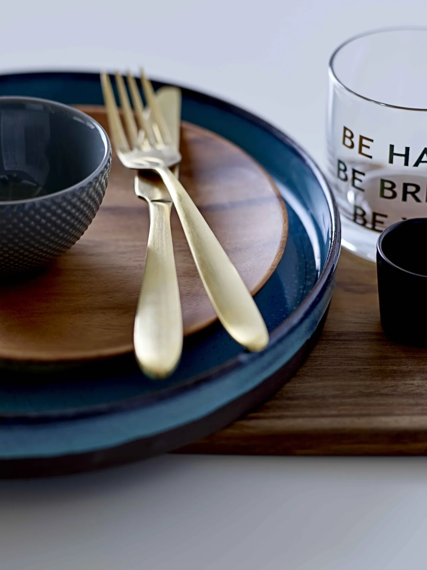 Place setting with a blue plate, wooden charger and gold cutlery