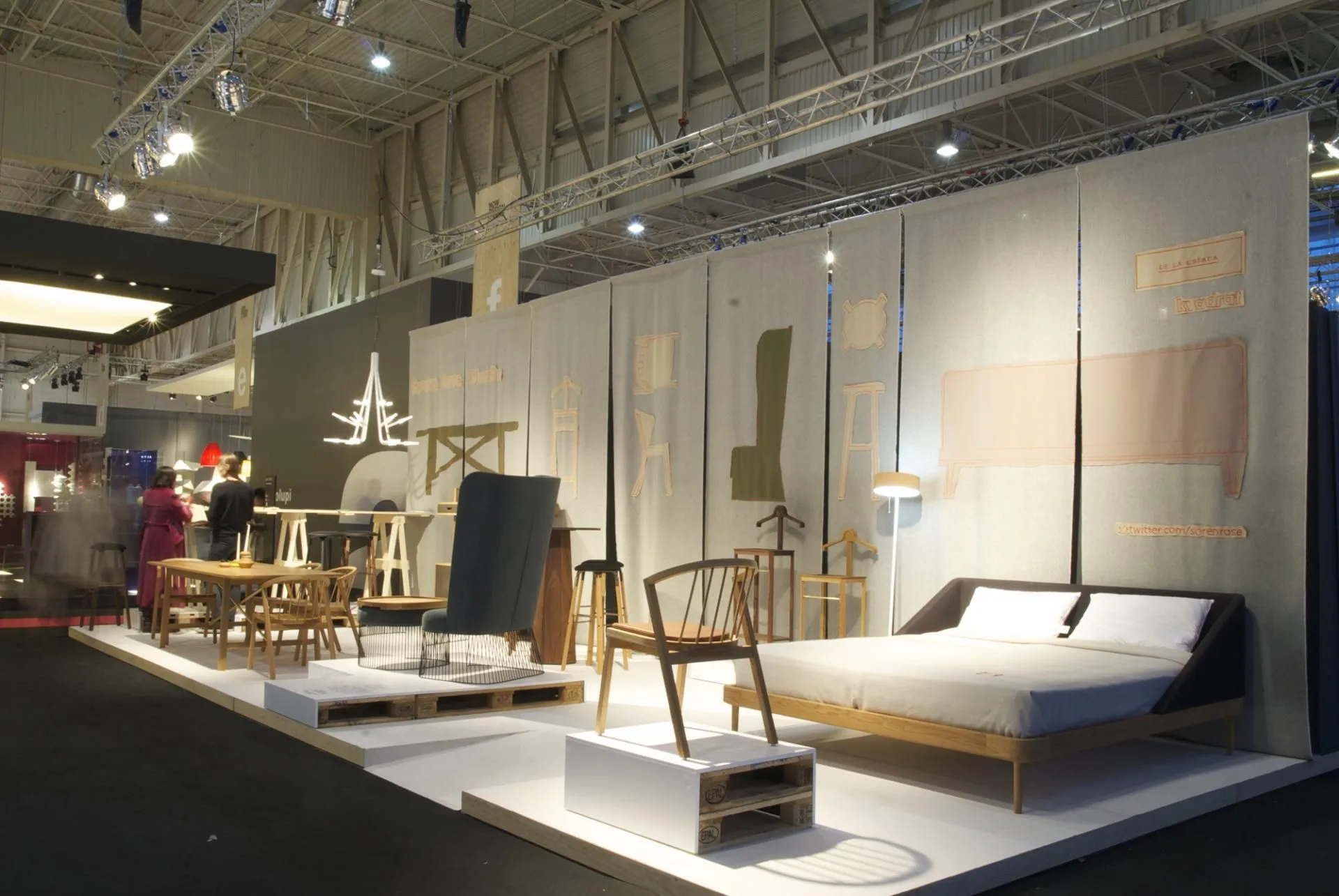 Messestand mit Bett, Holzstühlen und Einrichtungsobjekten auf einer Designmesse